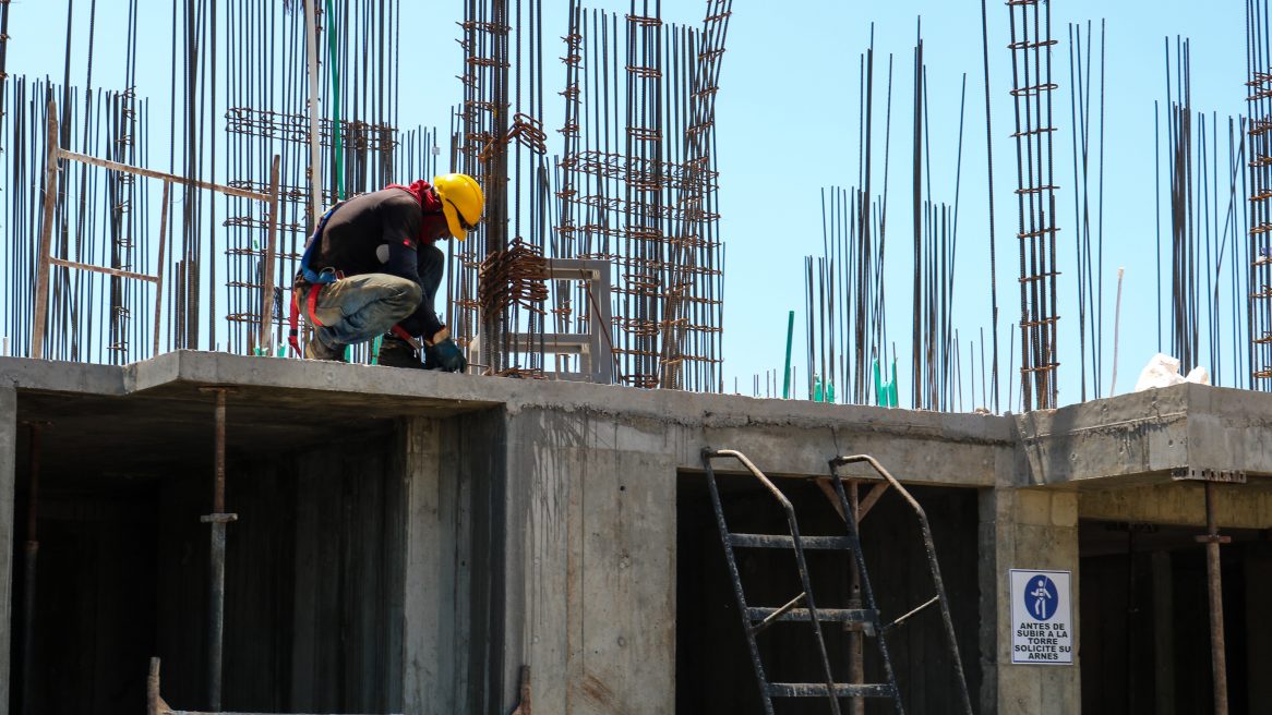 Ein Bauarbeiter mit Helm kniet auf einem unfertigen Bauwerk.